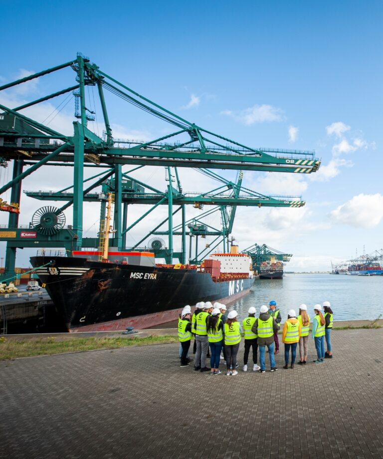 Studenten hoger onderwijs staan aan de kade in de haven en krijgen uitleg van een gids tijdens een havenbezoek. © Kris Jacobs