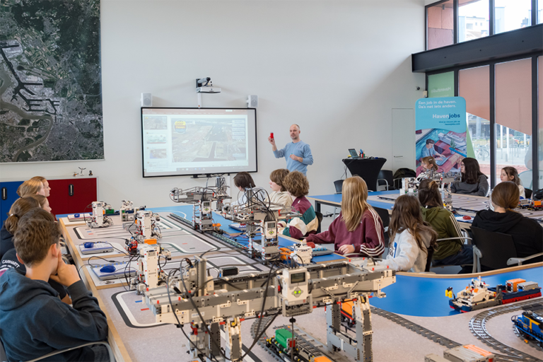 Een groep leerlingen van het secundair onderwijs zit aan tafel in de Havenstudio en krijgt uitleg van een educoach over de STEM-activiteit.