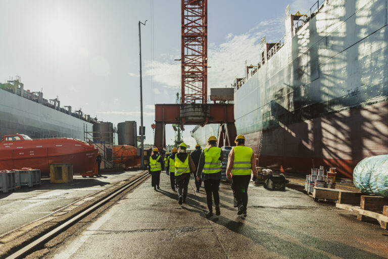 Een groep leerlingen van het secundair onderwijs loopt tussen de schepen in de havendokken tijdens een rondleiding.