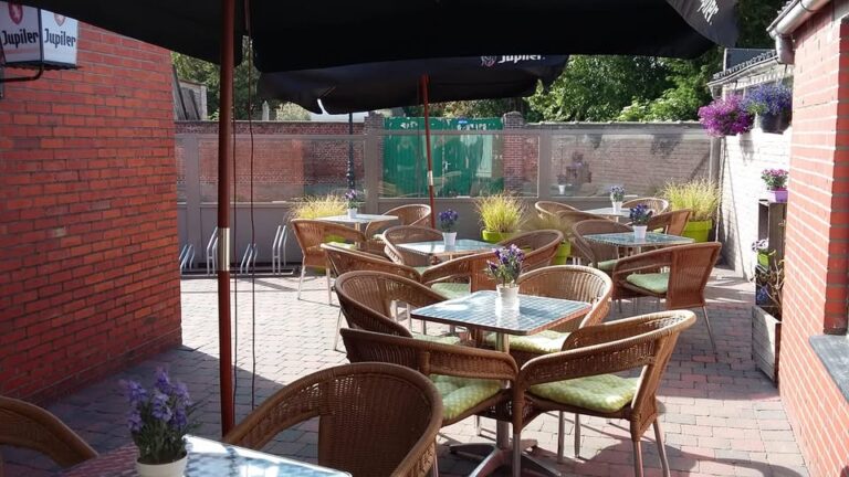 Foto van het terras aan Café Berendrecht Sport, met rieten terrasstoelen en kleine tafeltjes onder parasols.