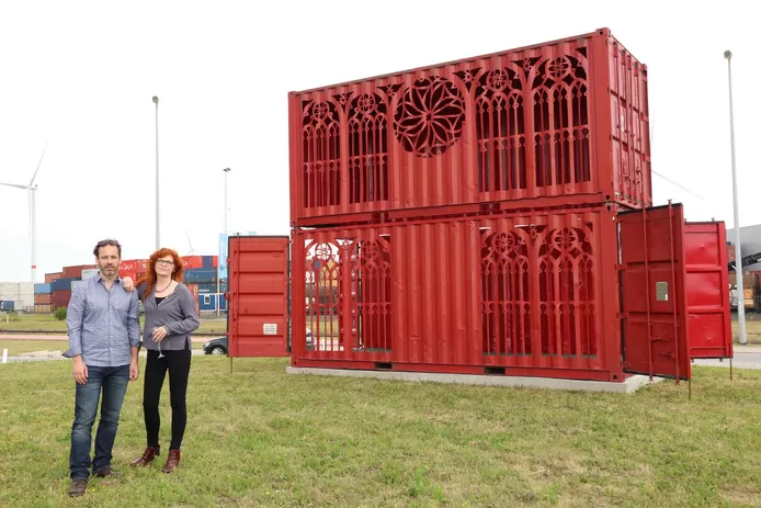 Twee artiesten staan voor hun kunstwerk: een rode containerkathedraal