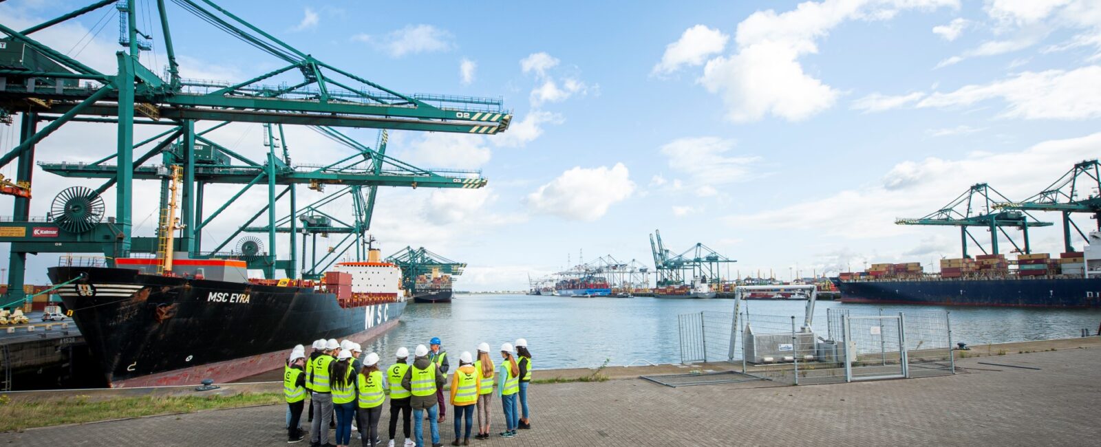 Studenten hoger onderwijs staan aan de kade in de haven en krijgen uitleg van een gids tijdens een havenbezoek. © Kris Jacobs