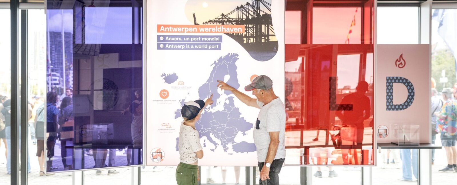 Een man en een kind staan voor een havenkaart en wijzen hier naar.