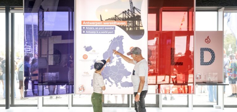 Een man en een kind staan voor een havenkaart en wijzen hier naar.