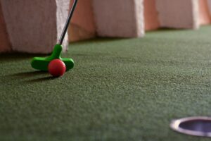 Close-up van een minigolf terrein met een groene golfclub en rood balletje.