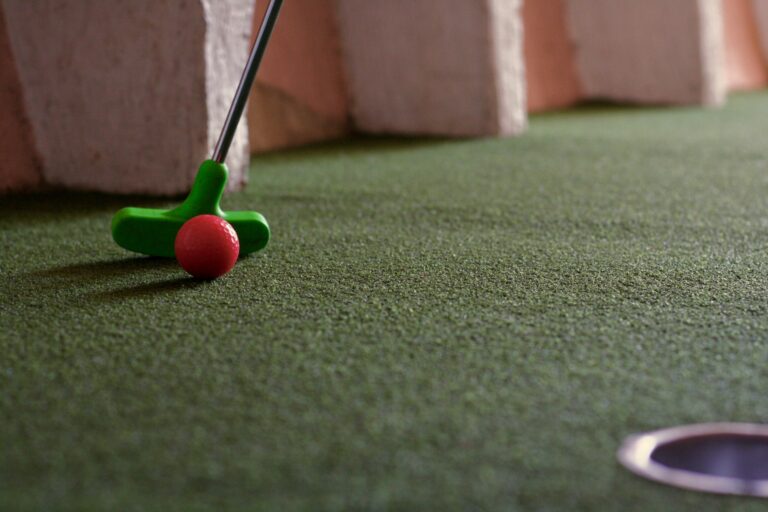 Close-up van een minigolf terrein met een groene golfclub en rood balletje.